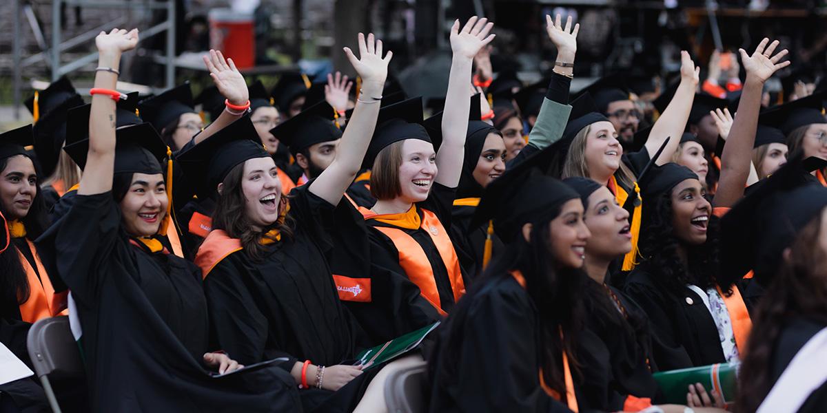 a crowd of graduates raising their hands during commencement